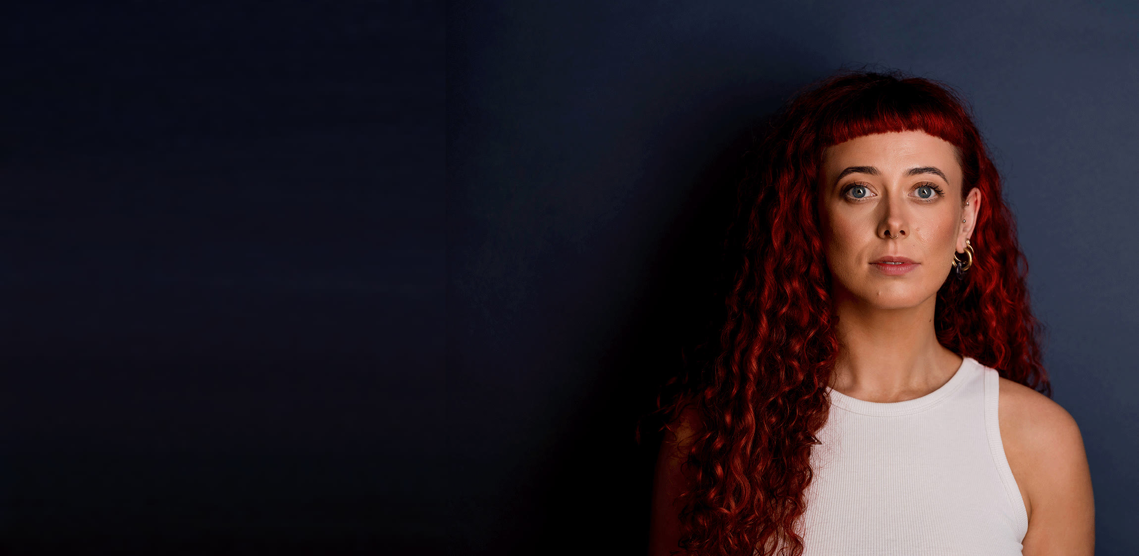 Emily Lamey, red curly hair, photographed against a deep navy studio backdrop.
