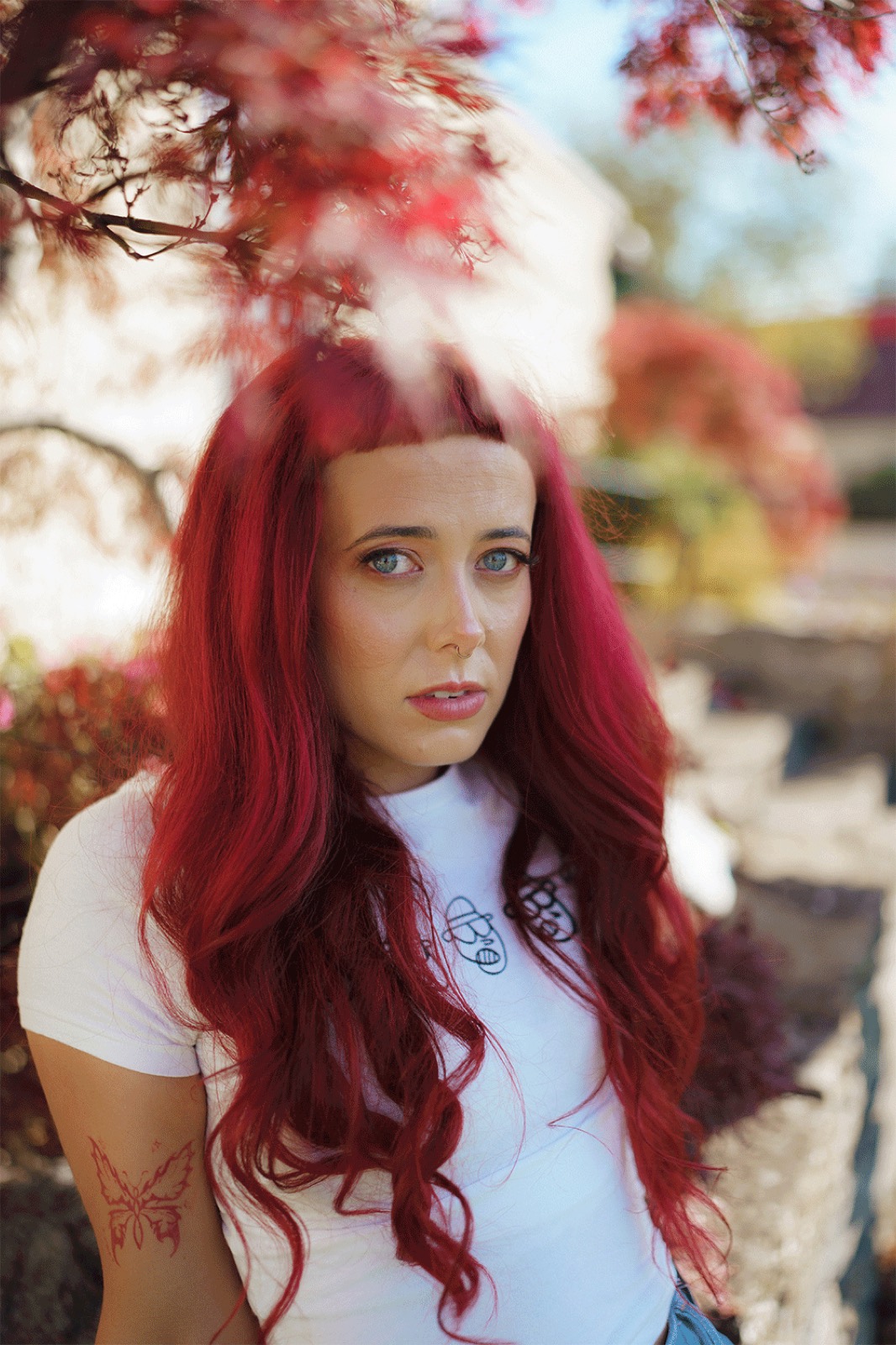 Emily Lamey in a white T-shirt beneath red maple leaves.