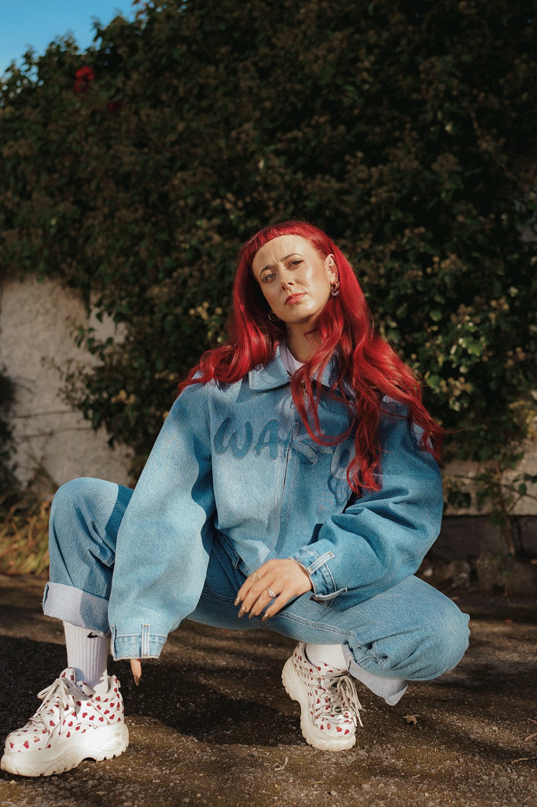 Emily Lamey crouching in a denim co-ord against a sunlit wall.