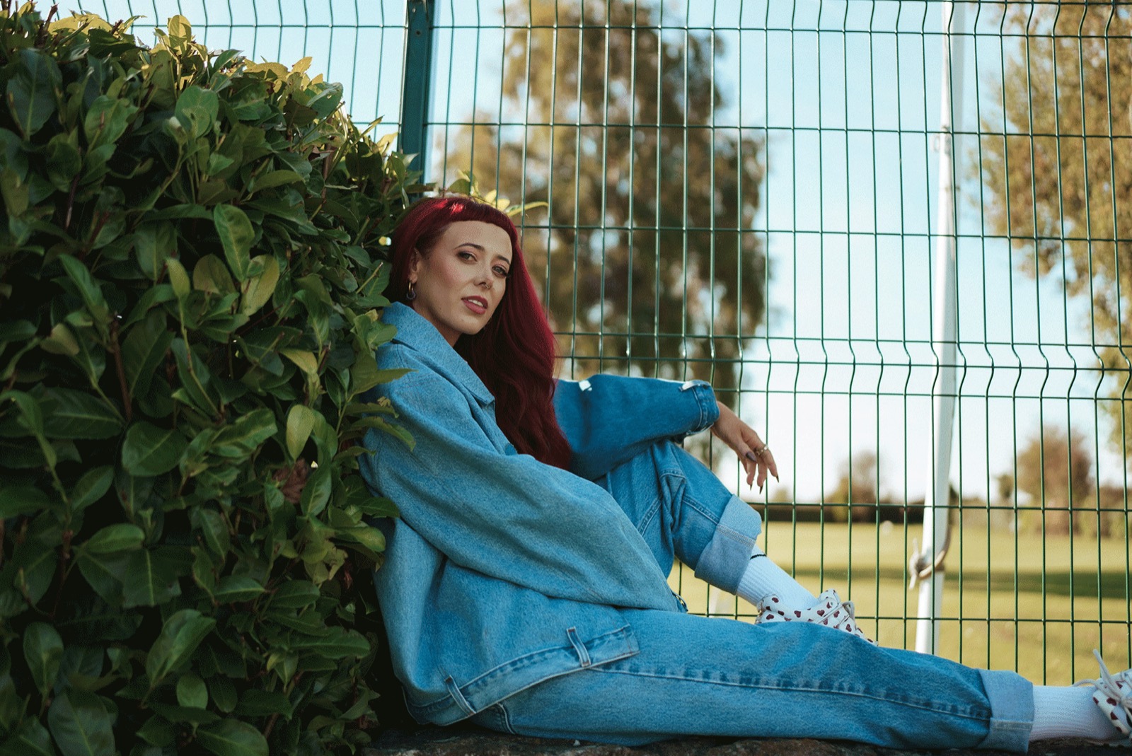 Emily Lamey seated against a hedge in denim.